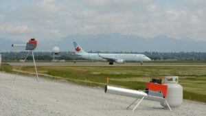 Air Canada aircraft taxiing on runway with monitoring equipment in foreground and mountains in background.